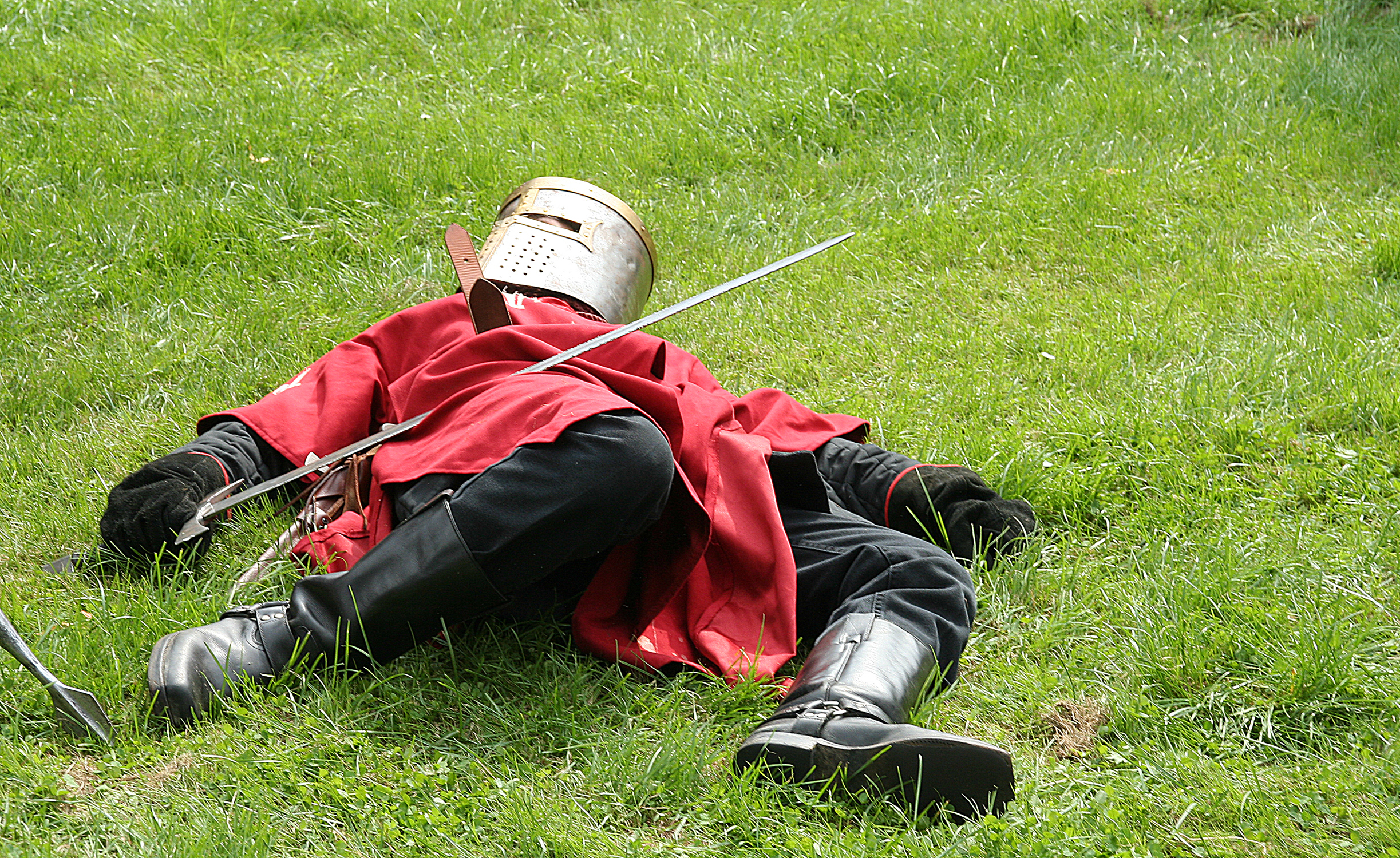 A dead knight character lies upon grass, their sword held in the right hand as they are sprawled upon the field.