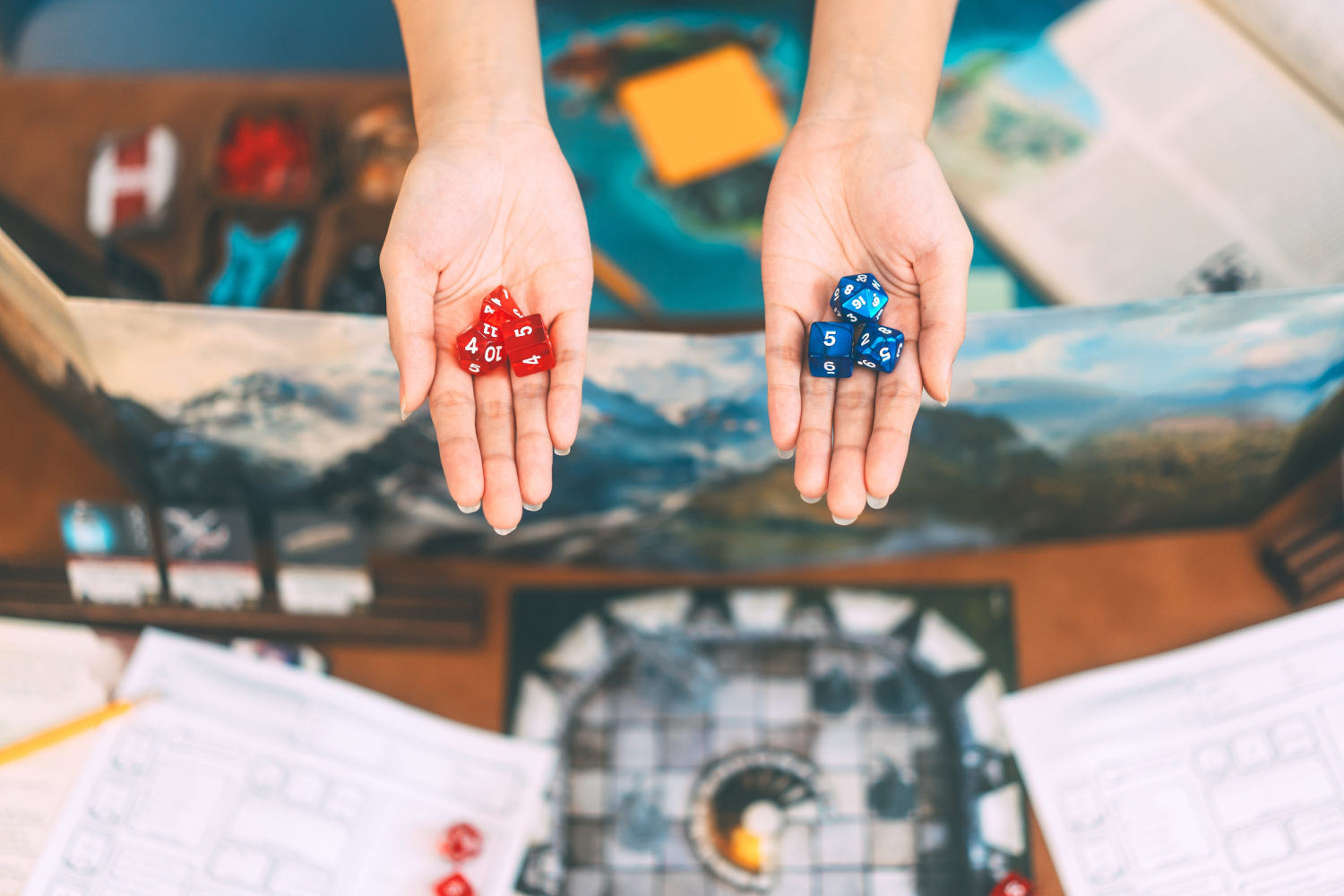 ands reaching in from top, palms up. One holds red dice, the other holds blue dice. In the background are old D&D materials.