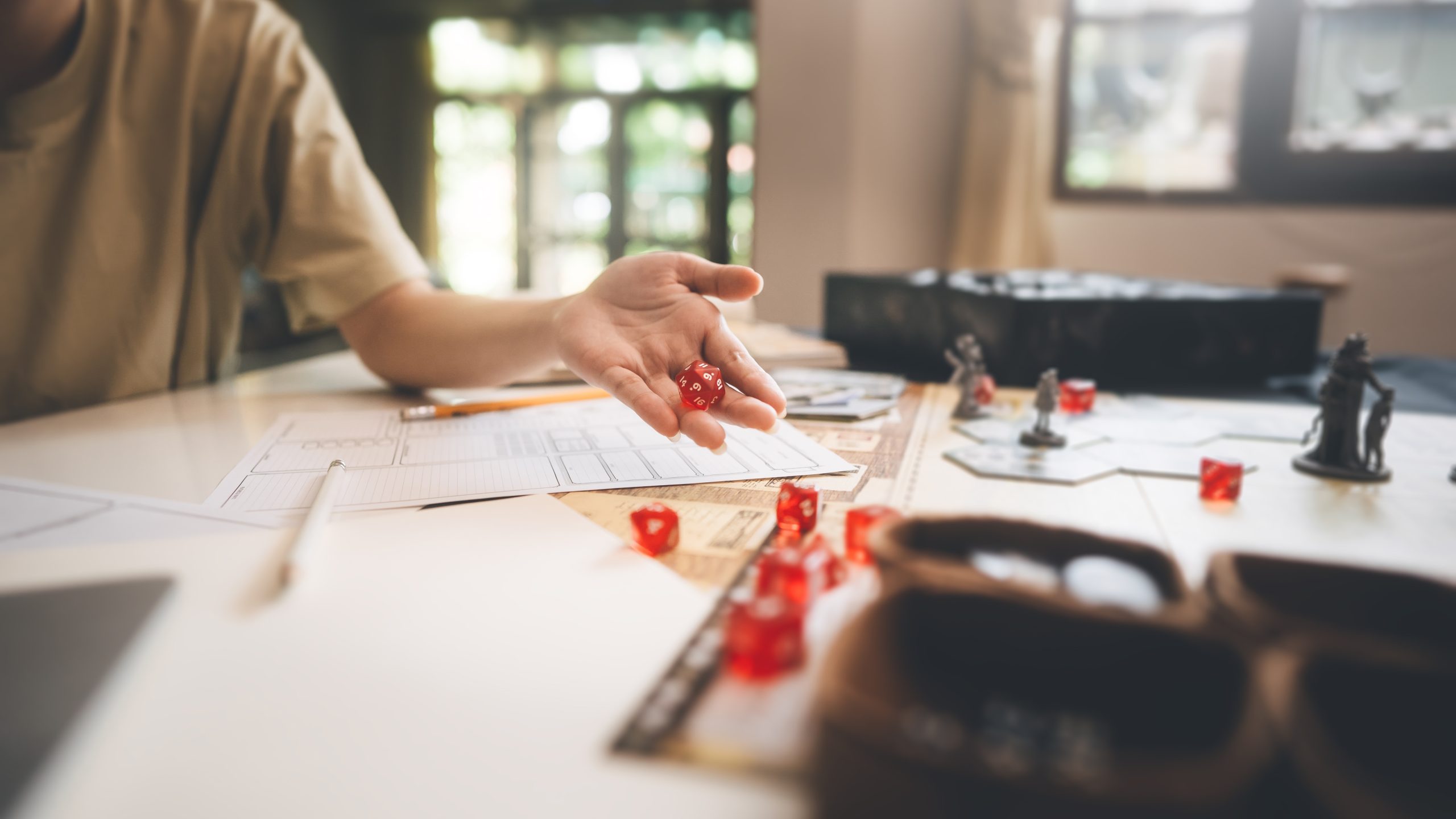An OSR gamer rolls dice on a table with miniatures, rules, and character sheets.